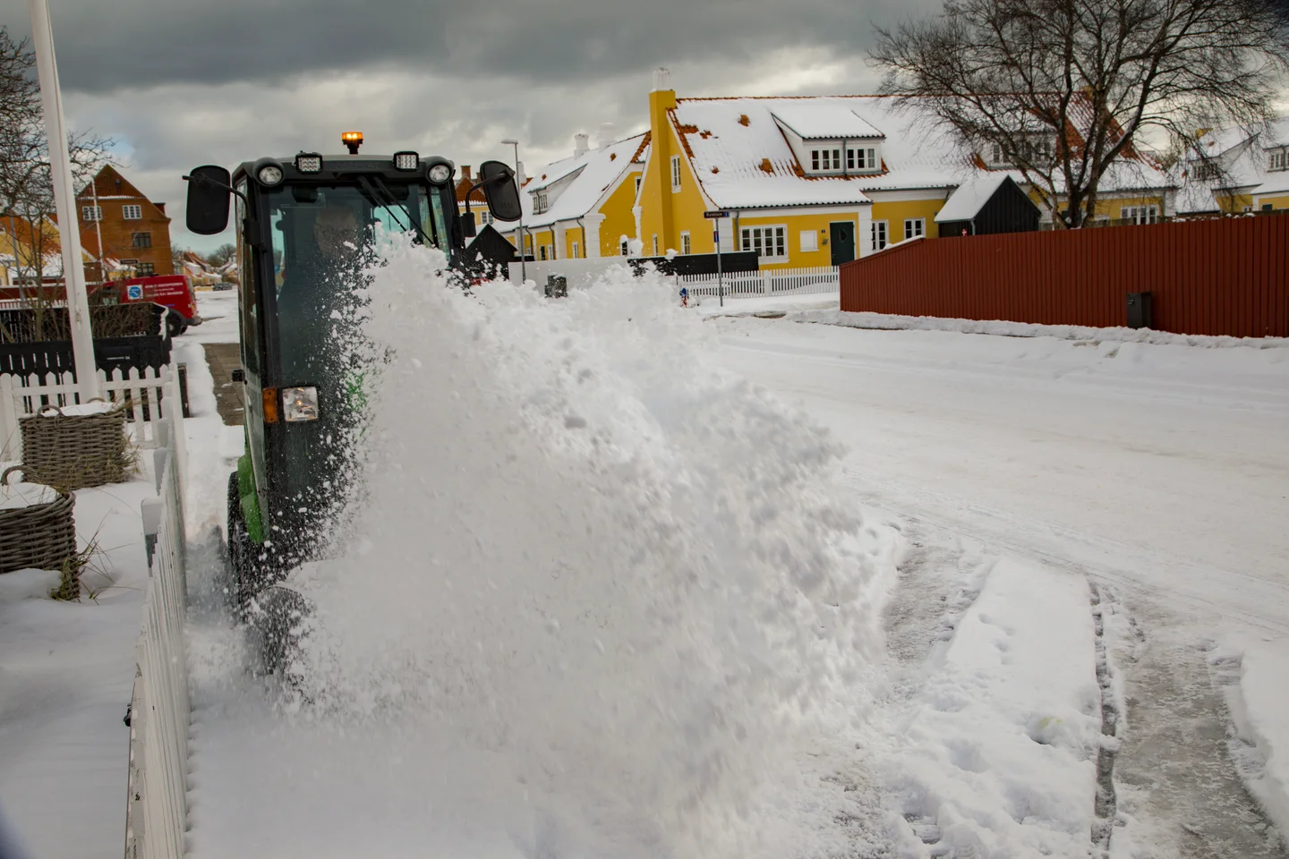 Snerydningsmaskine rydder sne langs et fortov foran snedækkede huse